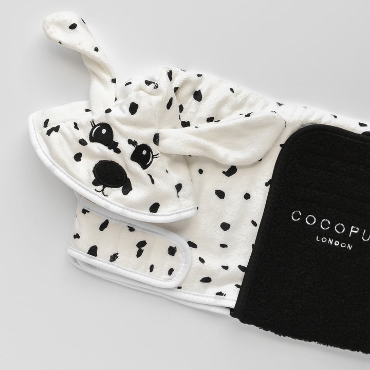 A neatly folded black and white spotted, dog-themed garment featuring floppy ears and a cute face lies next to a premium microfibre Dalmatian Drying Robe by Cocopup London. The vivid details stand out beautifully against the white background.