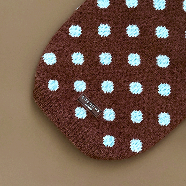 A close-up of a brown knit dog jumper with pale blue polka dots, showing the Cocopup London logo, on a solid beige background.