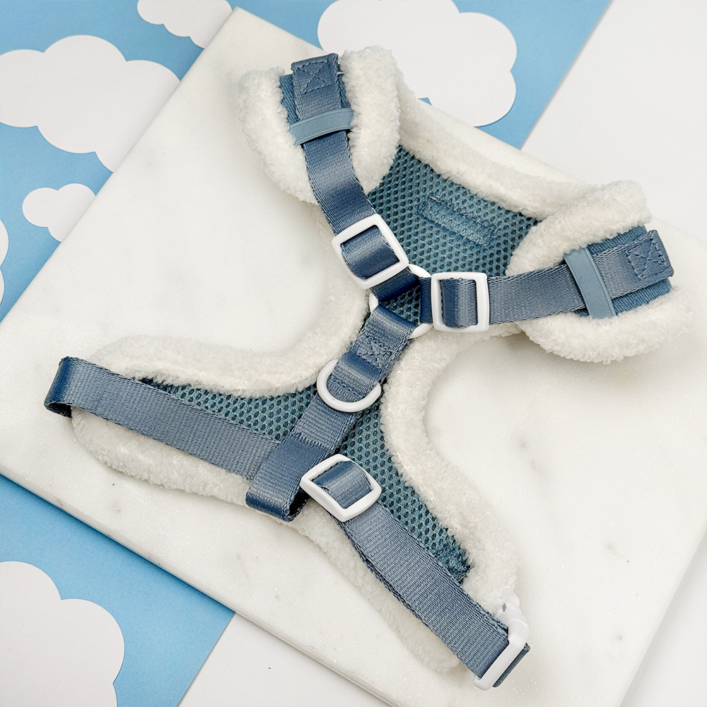 Blue denim dog harness with white fleece lining on a blue and white cloud-patterned background