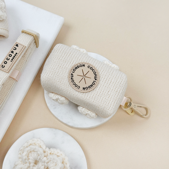 Beige knitted pouch with beige metal clip and hole to put poop bags through.