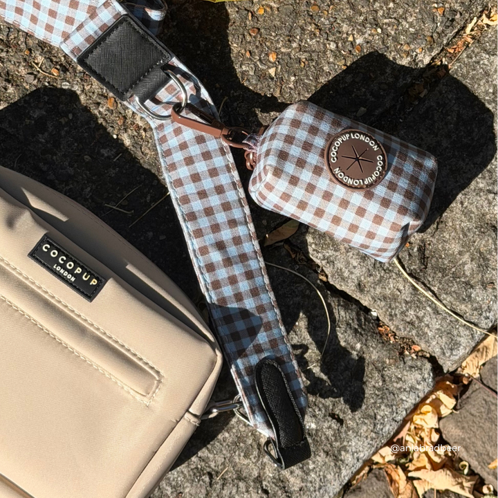 a beige crossbody bag with a blue and brown gingham strap and matching poop bag holder