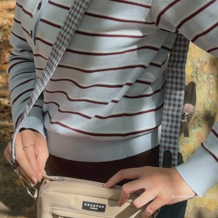 a women is wearing a beige crossbody bag with a blue and brown gingham strap and matching poop bag holder