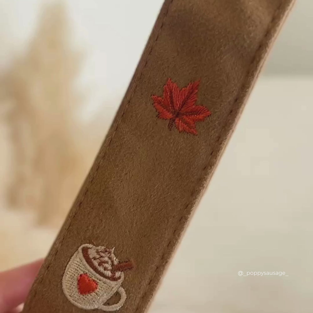 Close-up of tan suede strap featuring embroidered red and orange mushrooms and a leaf