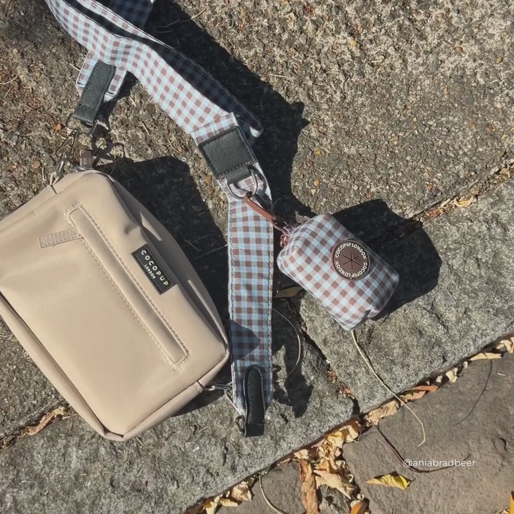 a beige crossbody bag with a blue and brown gingham strap and matching poop bag holder