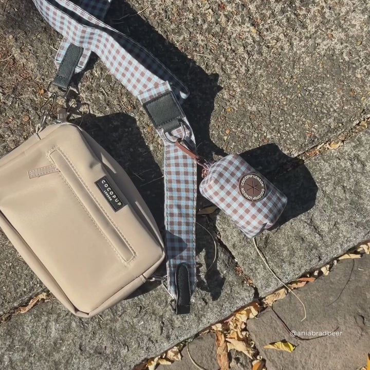 a beige crossbody bag with a blue and brown gingham strap and matching poop bag holder