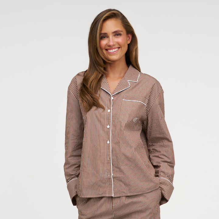 A woman wearing a brown and beige vertically striped pajama set with white piping, photographed against a clean light gray studio background.